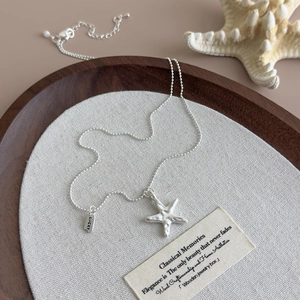 Detail of blue starfish pendant and bead chain with Lucky tag on a wooden tray