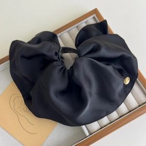 Detail view of a large black pleated satin hair claw clip with a gold metal accent