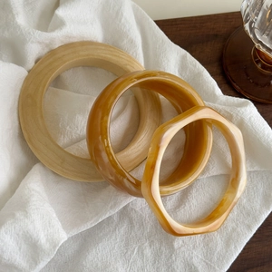 Empilement de bracelets en bois et résine ambrée sur tissu doux avec lumière naturelle