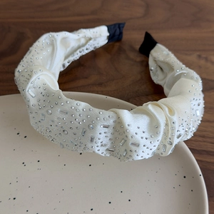 Dettaglio del cerchietto in raso crema con strass scintillanti su un vassoio di ceramica