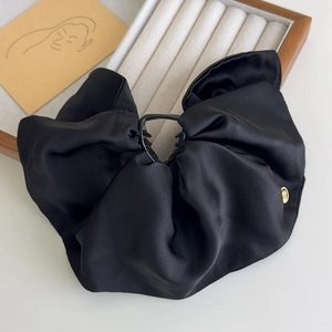 Detail of a large black satin bow hair claw clip with a subtle gold metal logo button