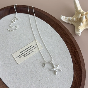Close-up of a silver starfish pendant with a Lucky engraved tag on a layered bead chain