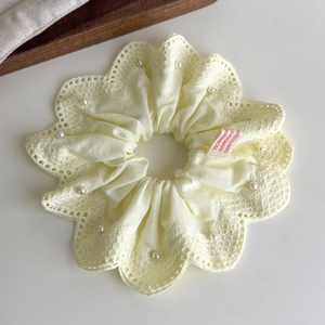 Détail d'un chouchou en dentelle crème avec perles blanches et étiquette rouge