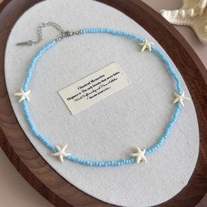 Detail of blue beaded necklace with white starfish pendants on an oval wooden tray