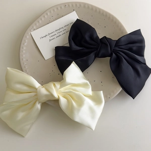 Close-up of elegant cream and black satin bow hair clips on a decorative ceramic plate