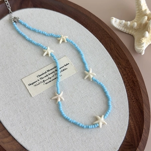Detailed close-up of blue bead necklace with white starfish charms in a wooden tray