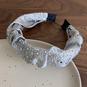 Dettaglio di cerchietto in seta argento con strass su vassoio in ceramica beige