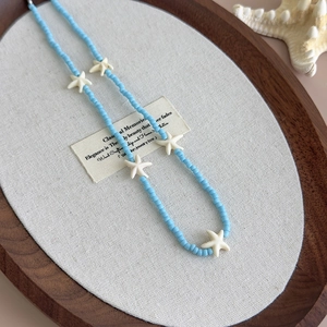 Detailed close-up of blue beaded necklace with white starfish charms on a wooden tray