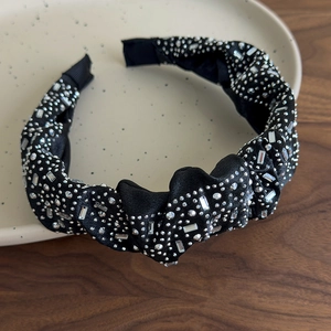 Dettaglio di cerchietto in raso nero plissettato con strass lucidi su vassoio beige