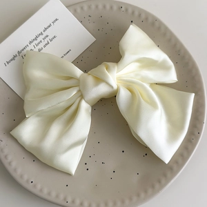 Close-up of elegant cream white satin bow hair clip with smooth silk texture and spring clip