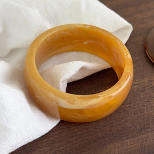 Détail d'un bracelet en résine ambre avec texture marbrée sur fond de lin blanc