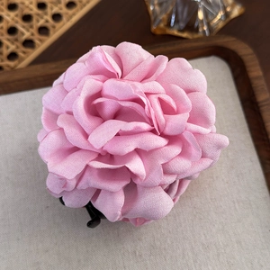 Detailansicht einer rosa mehrlagigen Stoffblumen-Haarklammer auf einem Holztablett