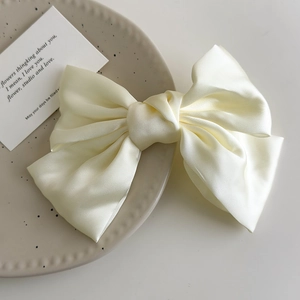 Detail shot of a cream satin bow hair clip with elegant glossy fabric texture