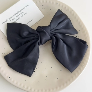 Detail view of a black satin bow hair clip on a minimalist ceramic display tray