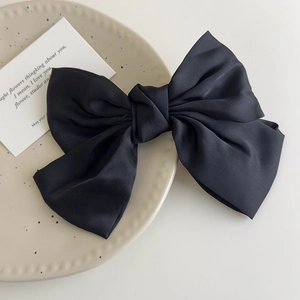 Detail of elegant black satin bow hair clip on a minimalist ceramic plate display