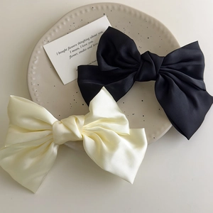 Elegant cream and black satin bow hair clips set on a decorative ceramic plate