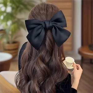 Elegant large black satin bow hair clip worn by a model in a cozy indoor setting
