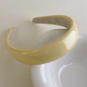 Detail of yellow glossy patent leather padded headband resting on white ceramic bowl