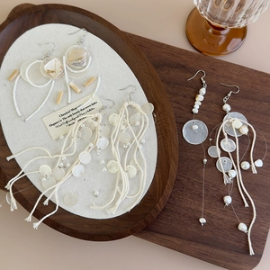 Long bohemian shell tassel earrings with white shells and pearls on a wooden tray