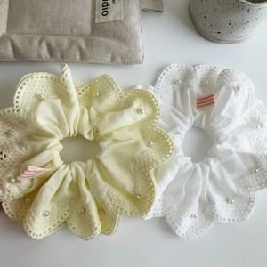 Détail de chouchous en dentelle avec broderie de perles blanches en jaune clair et blanc