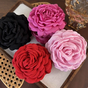 Haarklammern mit Blumen in Rot, Rosa und Schwarz auf einem Holztablett präsentiert