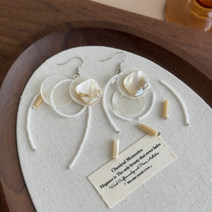 Detail of shell fringe earrings with white round disks and beaded tassels on linen background