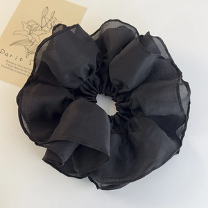 Close-up of black ruffled oversized scrunchie made of sheer chiffon fabric on white background