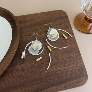 Detail view of long shell tassel earrings with white beads on a wooden tray