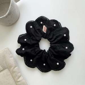 Détail d'un chouchou noir en tissu avec bordure en dentelle et perles sur fond blanc