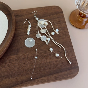 Detail of long shell tassel earrings with pearls on a rustic wooden tray for beach vacations