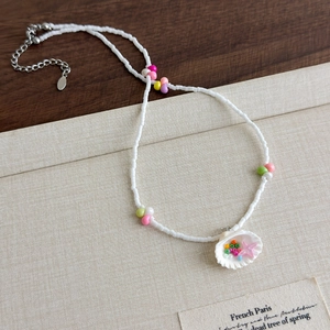 Détail du collier de perles avec pendentif coquillage, breloques étoiles et chaîne dorée