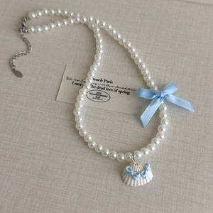 Détail du collier de perles avec un nœud en soie bleu clair et un pendentif coquillage