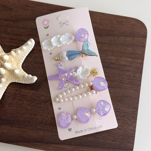 Détail de 5 barrettes sirène et coquillage violettes sur un fond en bois brun