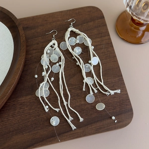 Detail of long bohemian shell fringe earrings with white cotton tassels on wooden tray