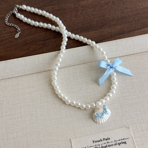 Détail du collier de perles avec un nœud en soie bleu clair et un pendentif coquillage