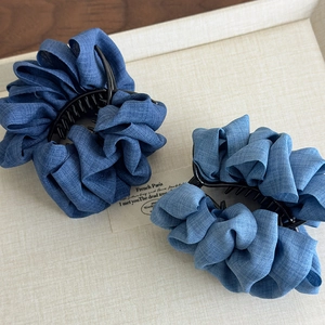 Set of two denim fabric ruffled claw clips in light blue on a textured display tray
