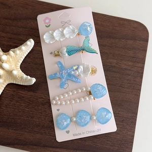 Détail de cinq barrettes marines avec étoiles de mer, coquillages et perles sur carte