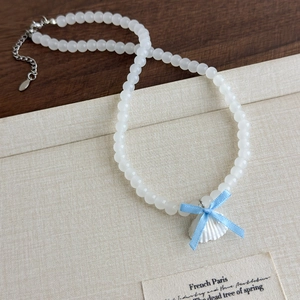 Détail du pendentif coquillage avec ruban bleu sur collier de perles blanches