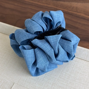 Detail shot of the denim blue pleated fabric bun clip on a neutral textured surface