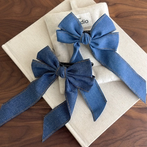 Detail of blue denim bow hair clips with orange stitching on a textured wooden background