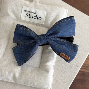 Detail of blue denim bow hair clip with yellow stitching and Hand Made leather label