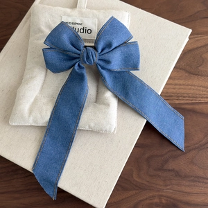 Detail of blue denim bow hair clip with vintage orange stitching and long ribbon