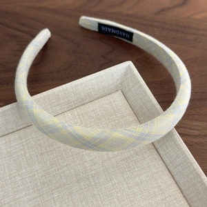 Detailed macro of yellow plaid fabric headband with handmade label on beige background