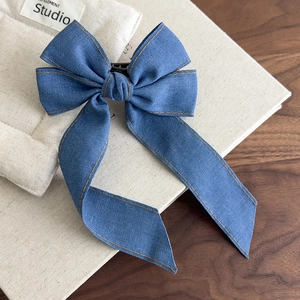 Detail of blue denim bow hair clip with orange stitching and long trailing ribbons