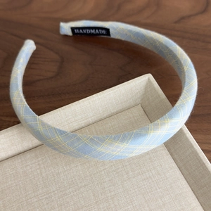Close-up of a blue checkered fabric headband with a handmade label on a beige tray