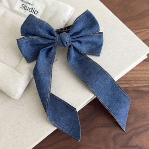 Close-up of denim bow hair clip with orange contrast stitching and metal duckbill clip
