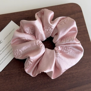 Dettaglio dello scrunchie in raso rosa con rose a rilievo su superficie in legno