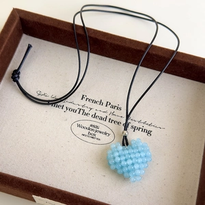 Vue macro d'un pendentif cœur en perles bleu clair avec cordon noir sur présentoir en toile