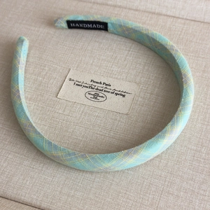 Detail of mint green plaid fabric headband with handmade tag on soft beige linen fabric