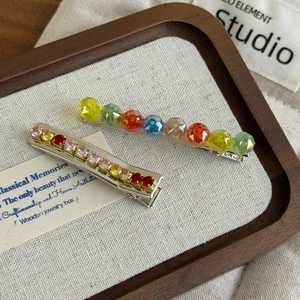 Colorful crystal hair clips with rainbow beads and rhinestones on a wooden tray